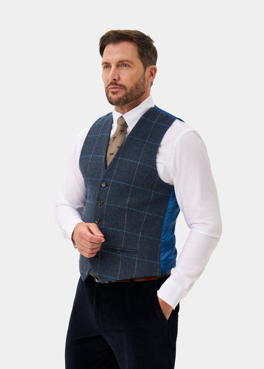 A man wears a Surrey Men’s Tweed Water Repellent Lined Waistcoat in Midnight Blue over a white dress shirt and tie.
