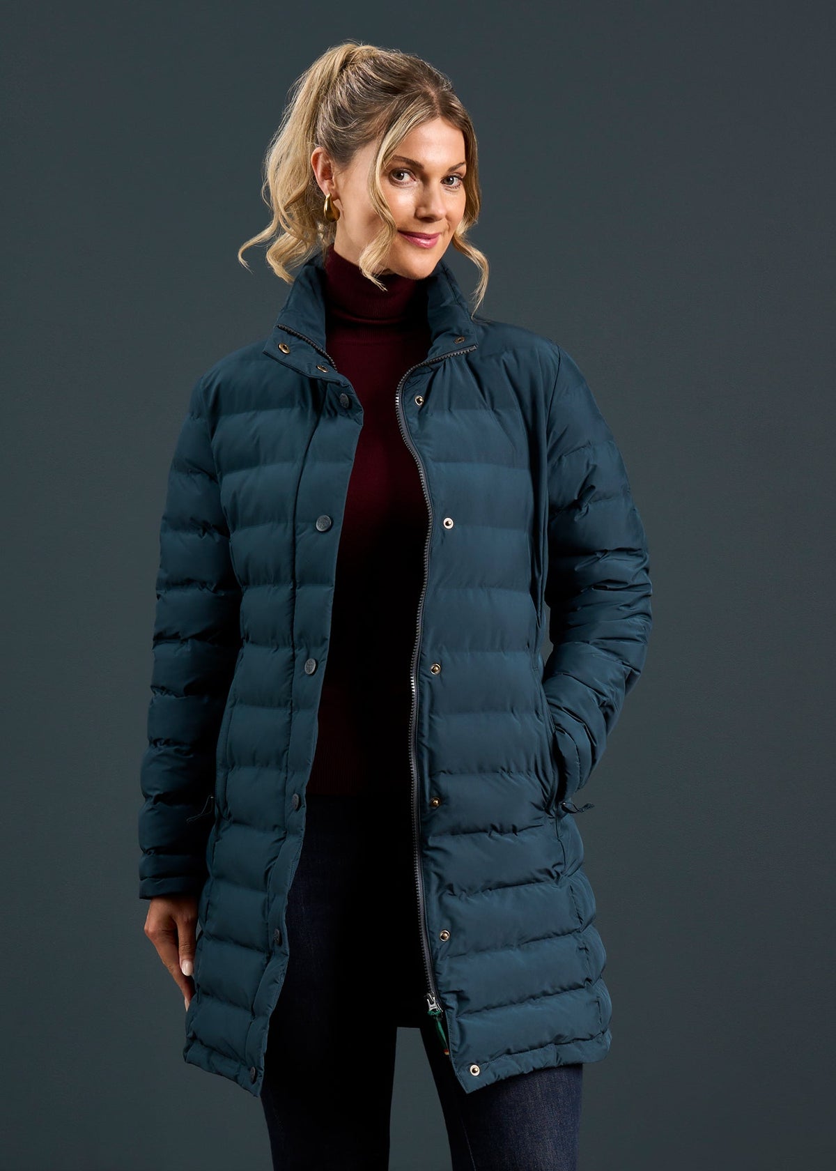 Woman in a navy Calsall Ladies Coat, regular fit, and burgundy turtleneck stands before a dark backdrop.