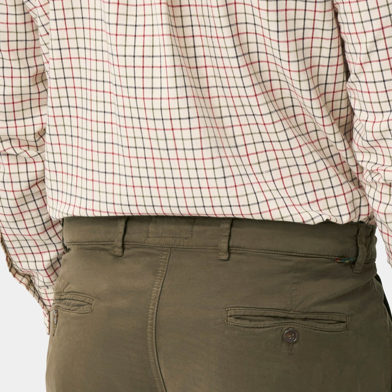 A man shown from the back wearing a beige and brown checkered long-sleeve button-down shirt and olive green trousers, against a light gray background.