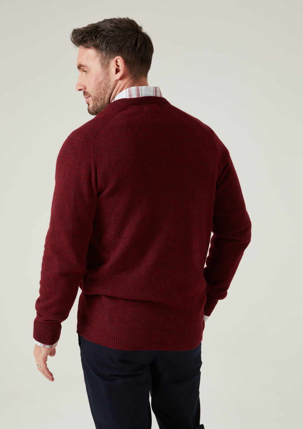 Man models the Hampshire Lambswool Vee Neck Jumper in Red Velvet, facing away and looking over his left shoulder.