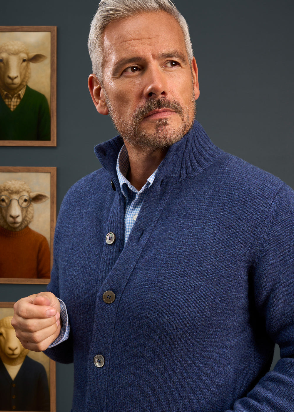 A man in a Landford Lambswool Buttoned Mock Neck Jumper stands by sheep art, gazing thoughtfully to the side.