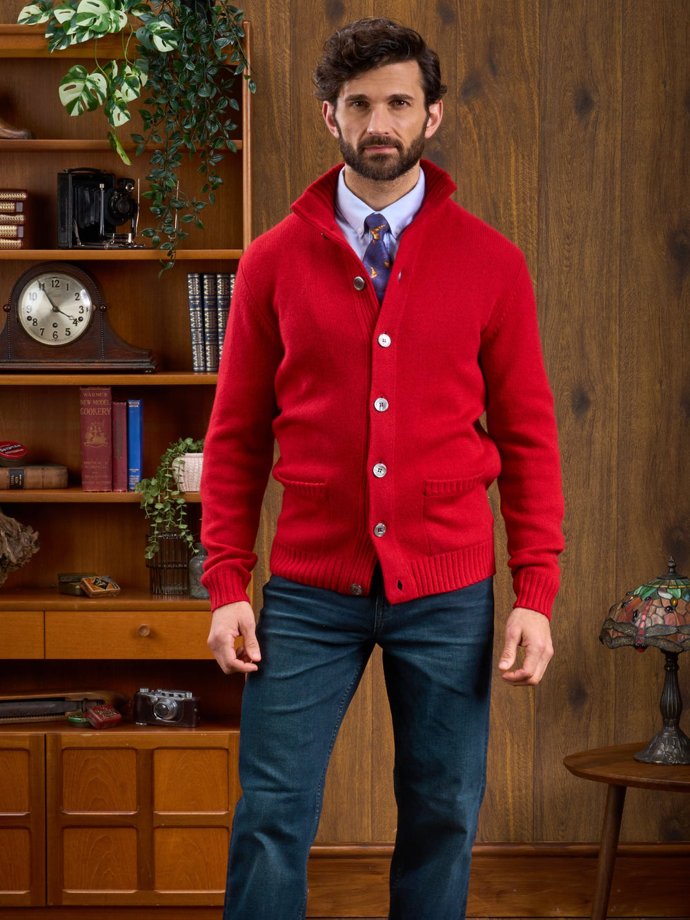 Man in a Landford Lambswool Mock Neck Jumper stands in a vintage room with wooden shelves and retro decor.