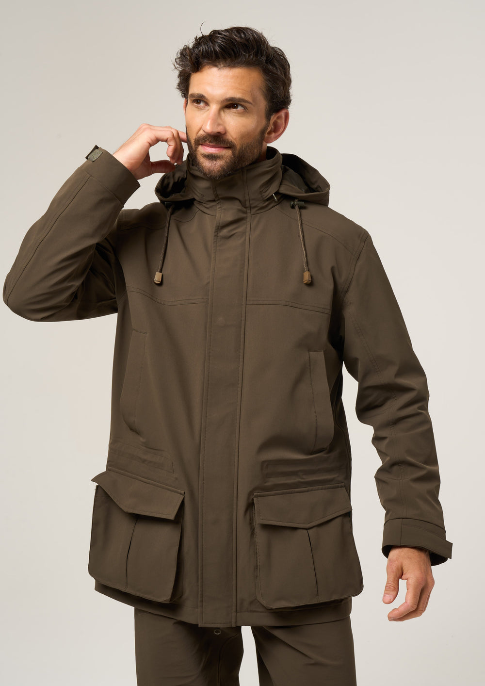 Man in olive Lockwood Men’s Shooting Coat - Shooting Fit, with front pockets, touching his ear against plain background.