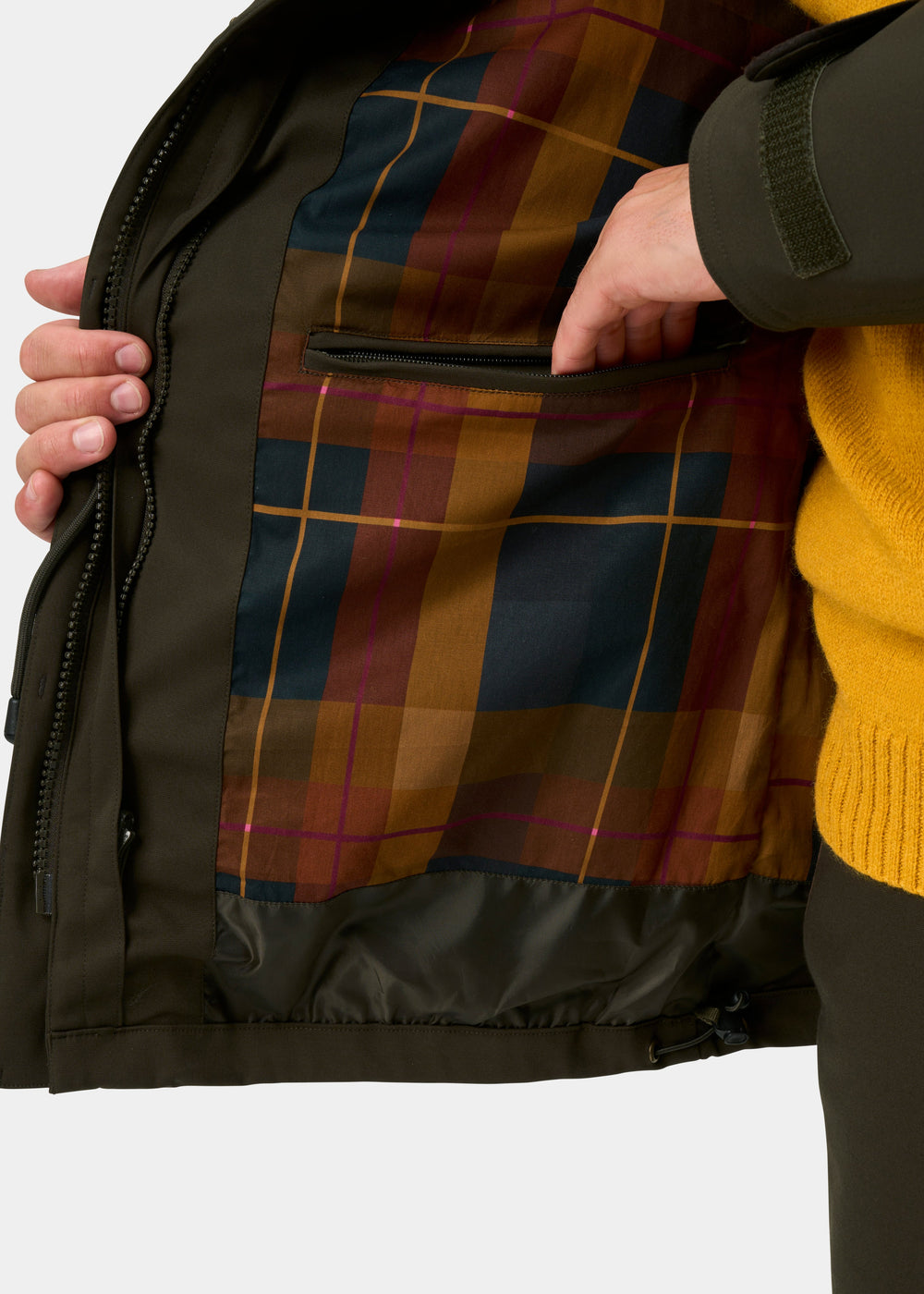 Dunswell Olive waterproof field coat opens to plaid lining with zip pocket; shooting fit, yellow sweater peeks out.