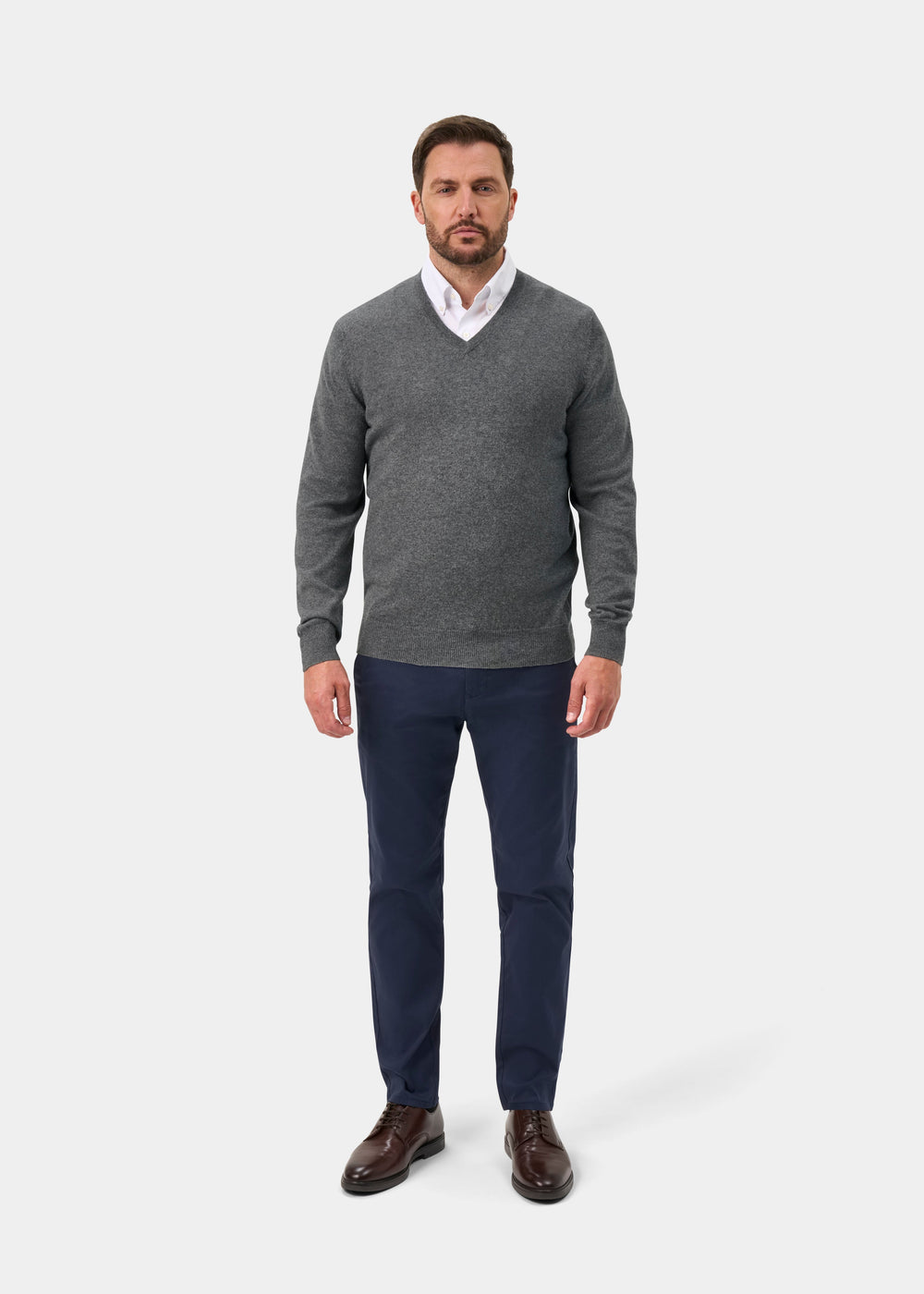 Man wears Haddington Pure Cashmere V-Neck Jumper in Derby, white shirt, navy pants, and brown shoes.