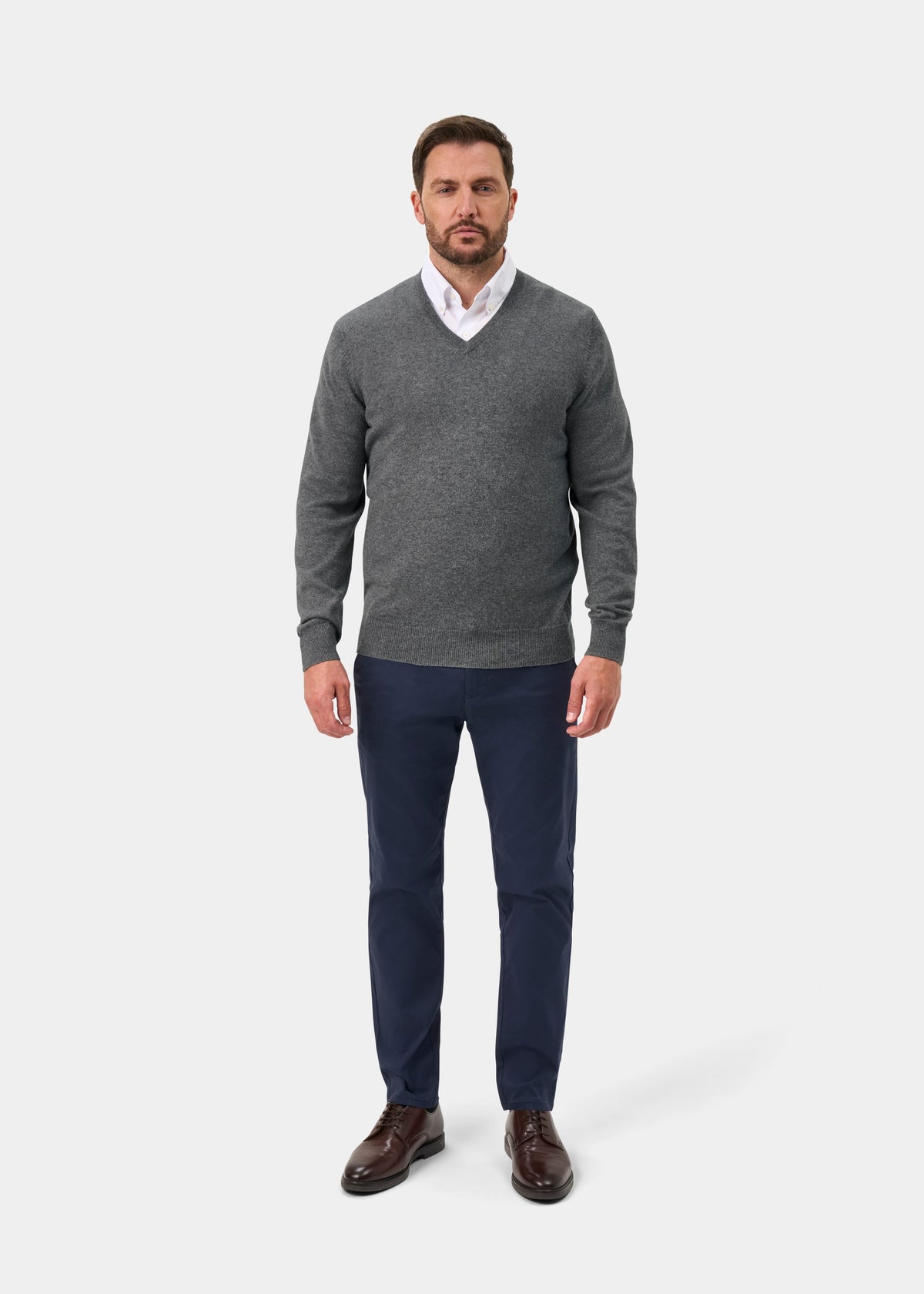 Man wears Haddington Pure Cashmere V-Neck Jumper in Derby, white shirt, navy pants, and brown shoes.