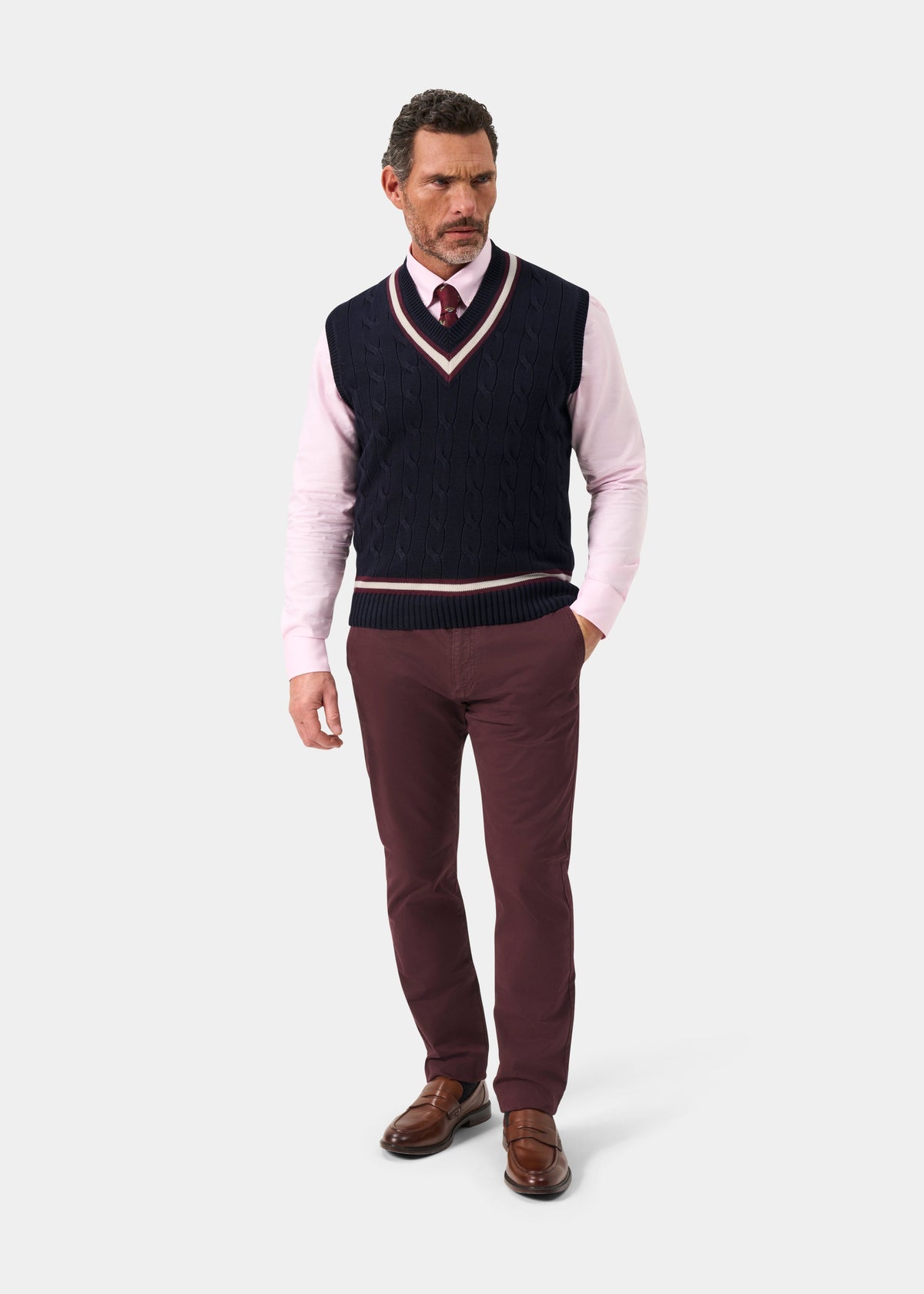 Man in Chadbury V-neck cricket slipover, pink shirt, burgundy tie and pants, brown shoes; on white background.