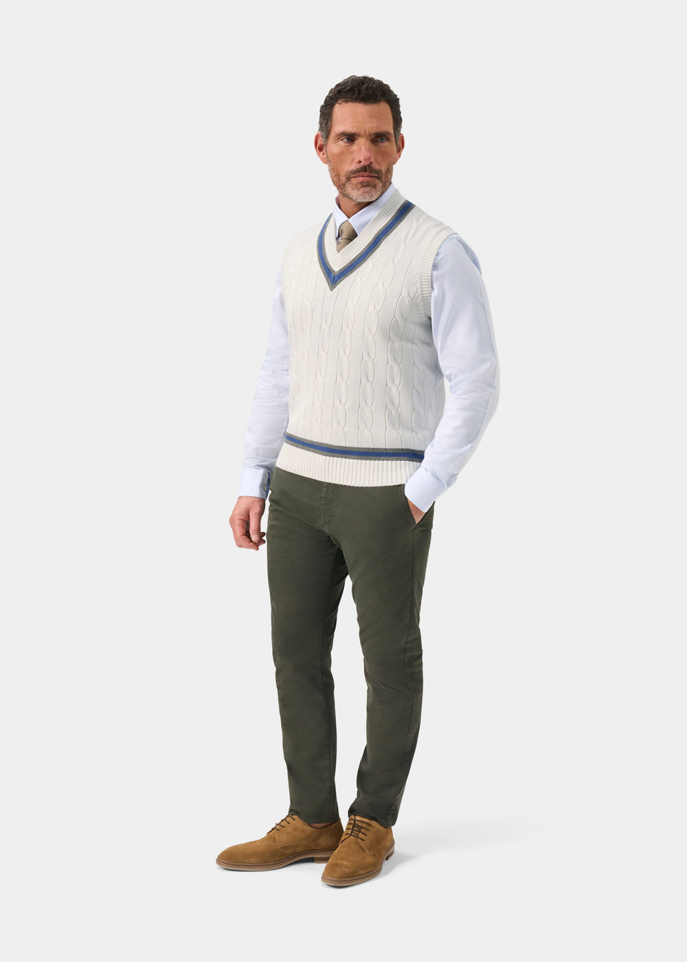 Man wears Chadbury Ecru & Landscape cable knit cricket slipover over a light blue shirt, with green pants and tan shoes.
