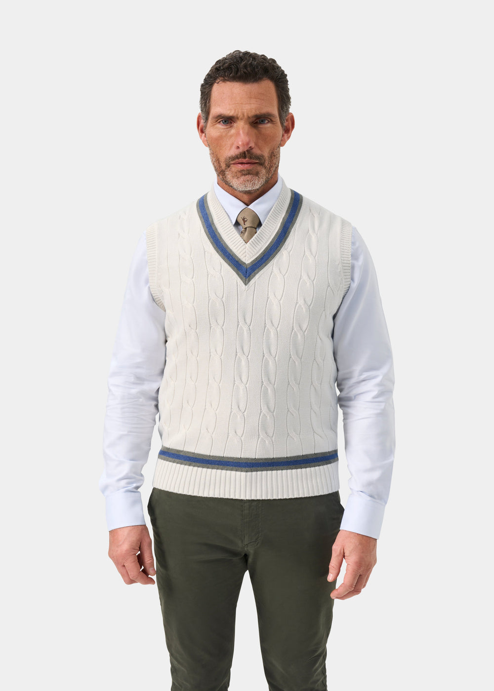 A man wears the Chadbury Ecru & Landscape cricket slipover, white shirt, tan tie, and olive green pants.