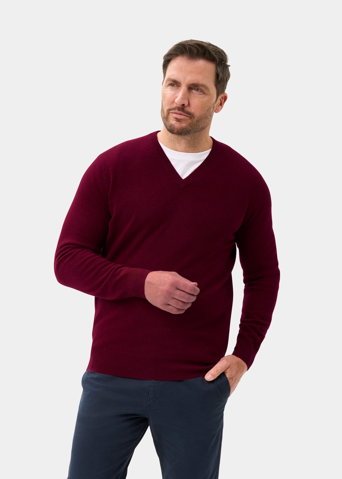 Man in Albury Geelong Wool V-Neck Jumper in Claret, regular fit, pairs it with navy pants against a light backdrop.