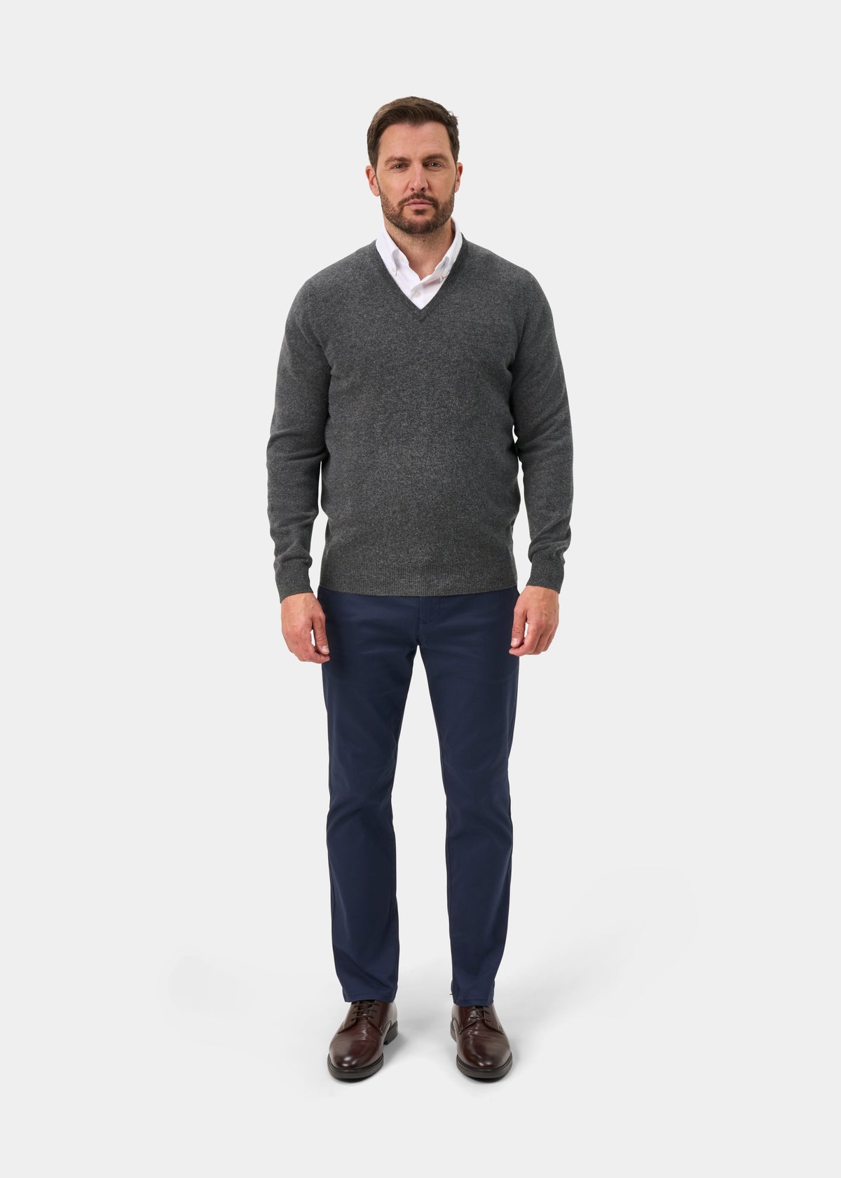 Man wearing Albury Geelong Wool V-Neck Jumper in Derby, white shirt, navy pants, and brown shoes.
