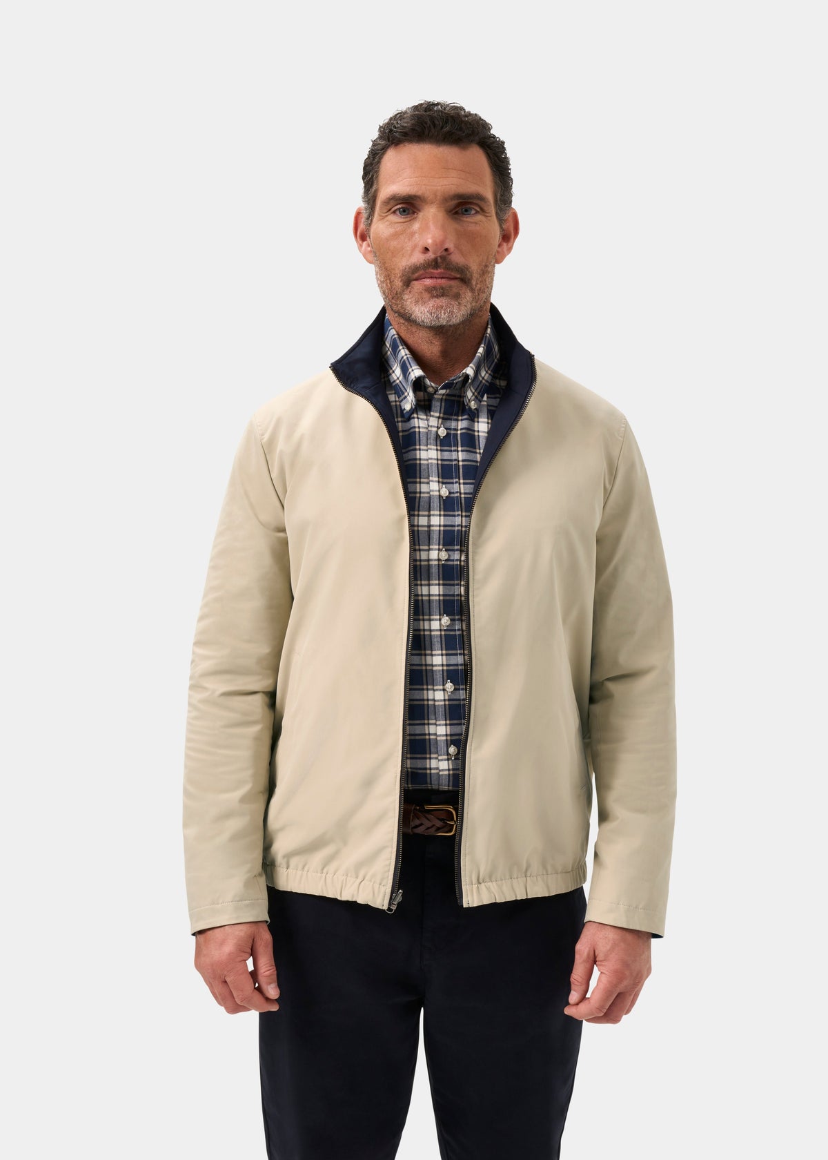 Man wearing Lakeward Men’s Reversible Bomber Jacket in navy over a plaid shirt and dark pants against white background.