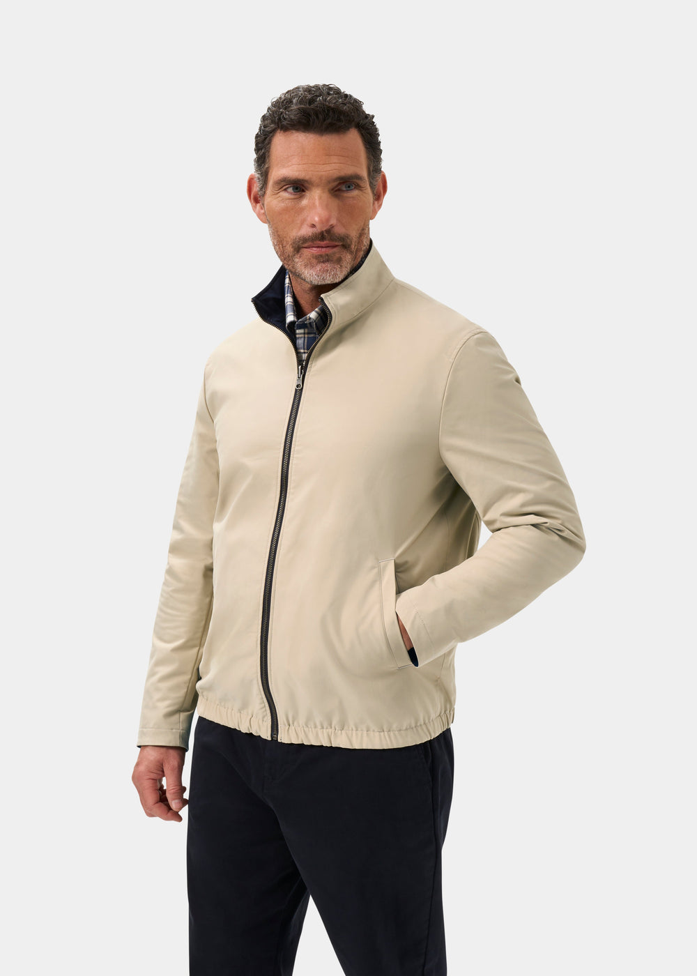 Man models Lakeward Men’s Reversible Bomber Jacket in Navy/Beige, hands in pockets, looking sideways, plain backdrop.