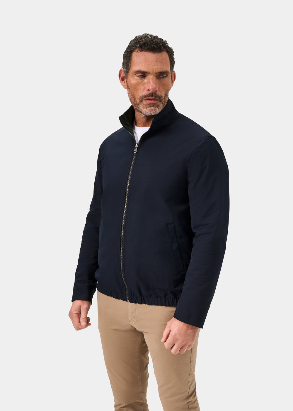 Man models Lakeward Men’s Reversible Bomber Jacket in Navy with beige pants, standing against a plain white background.