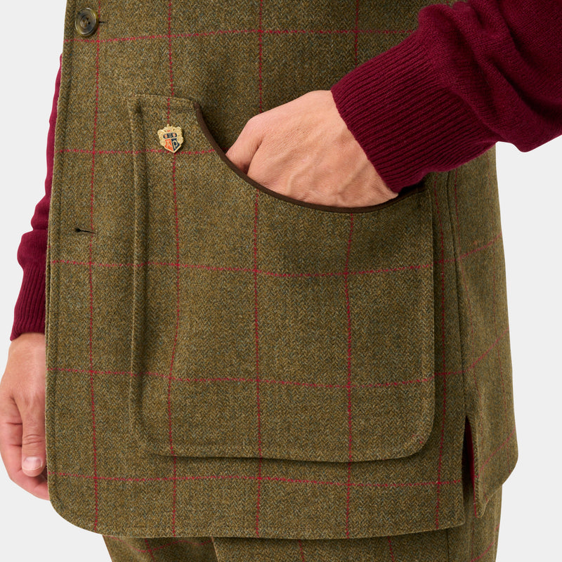 Close-up of a person wearing a brown tweed waistcoat with a red windowpane plaid pattern, a front flap pocket, and a burgundy knit sweater, against a light gray background.