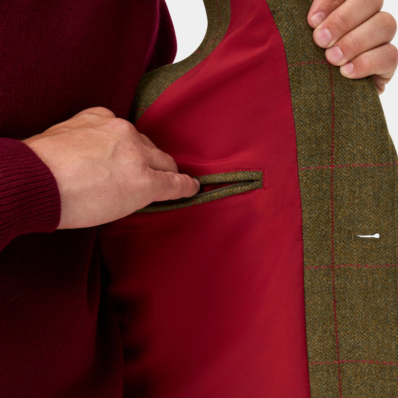 Close-up of a person wearing a burgundy knit sweater and holding open a green tweed jacket to show a matching green pocket lining.