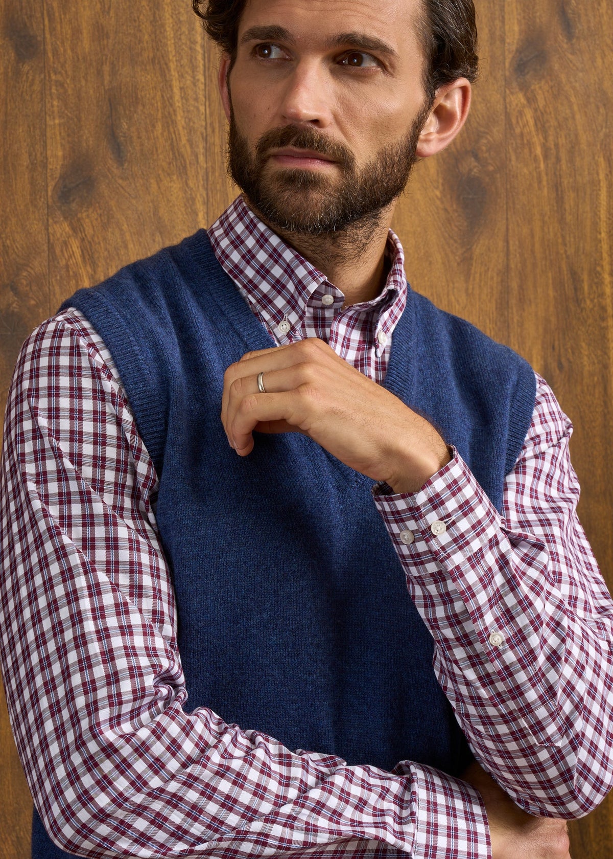 A man wears a Norfolk Lambswool V-Neck Slipover In Rhapsody over a red and white plaid button-down shirt.