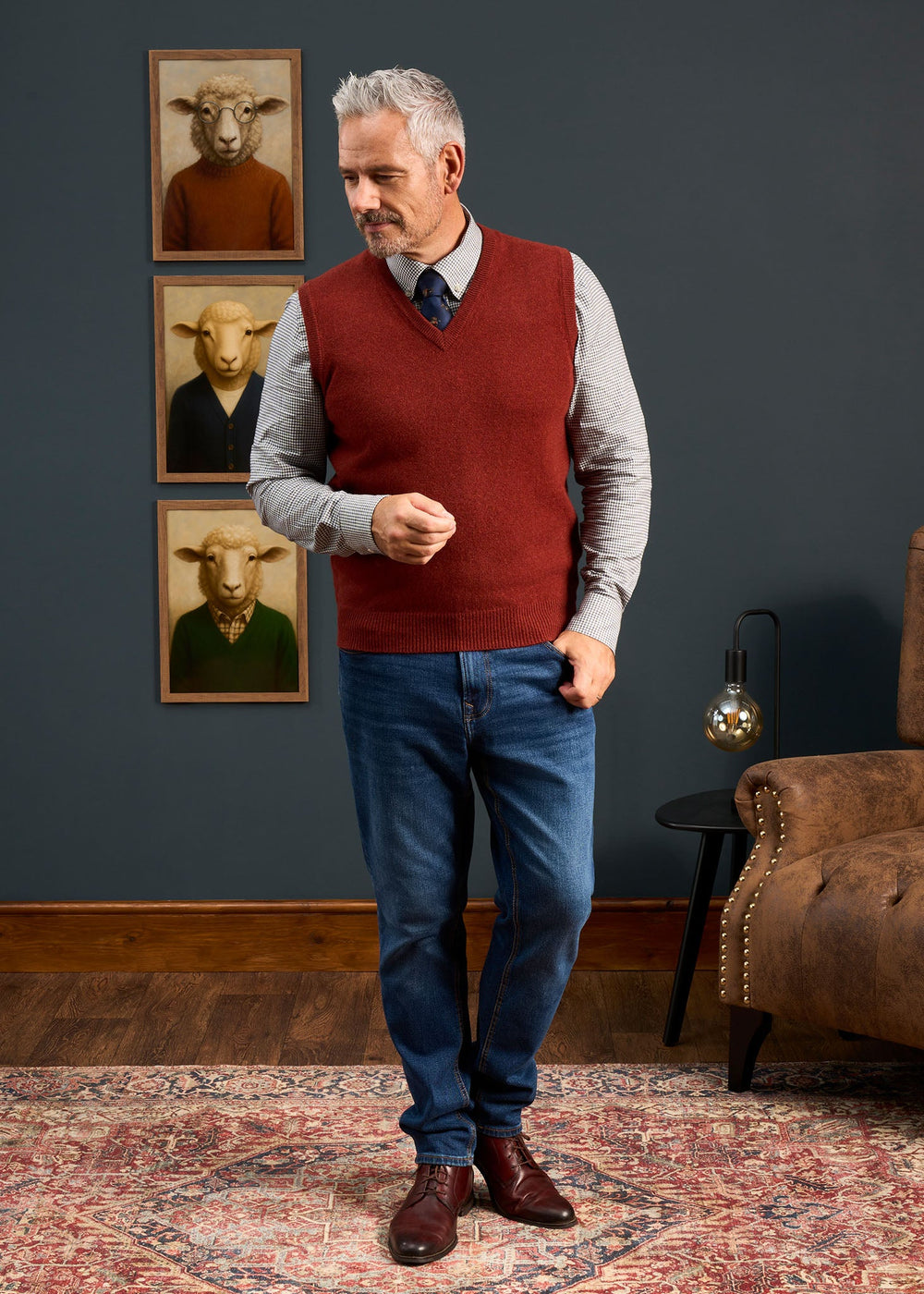 A man in a Norfolk Lambswool V-Neck Slipover In Sienna, a patterned dress shirt, and blue jeans.
