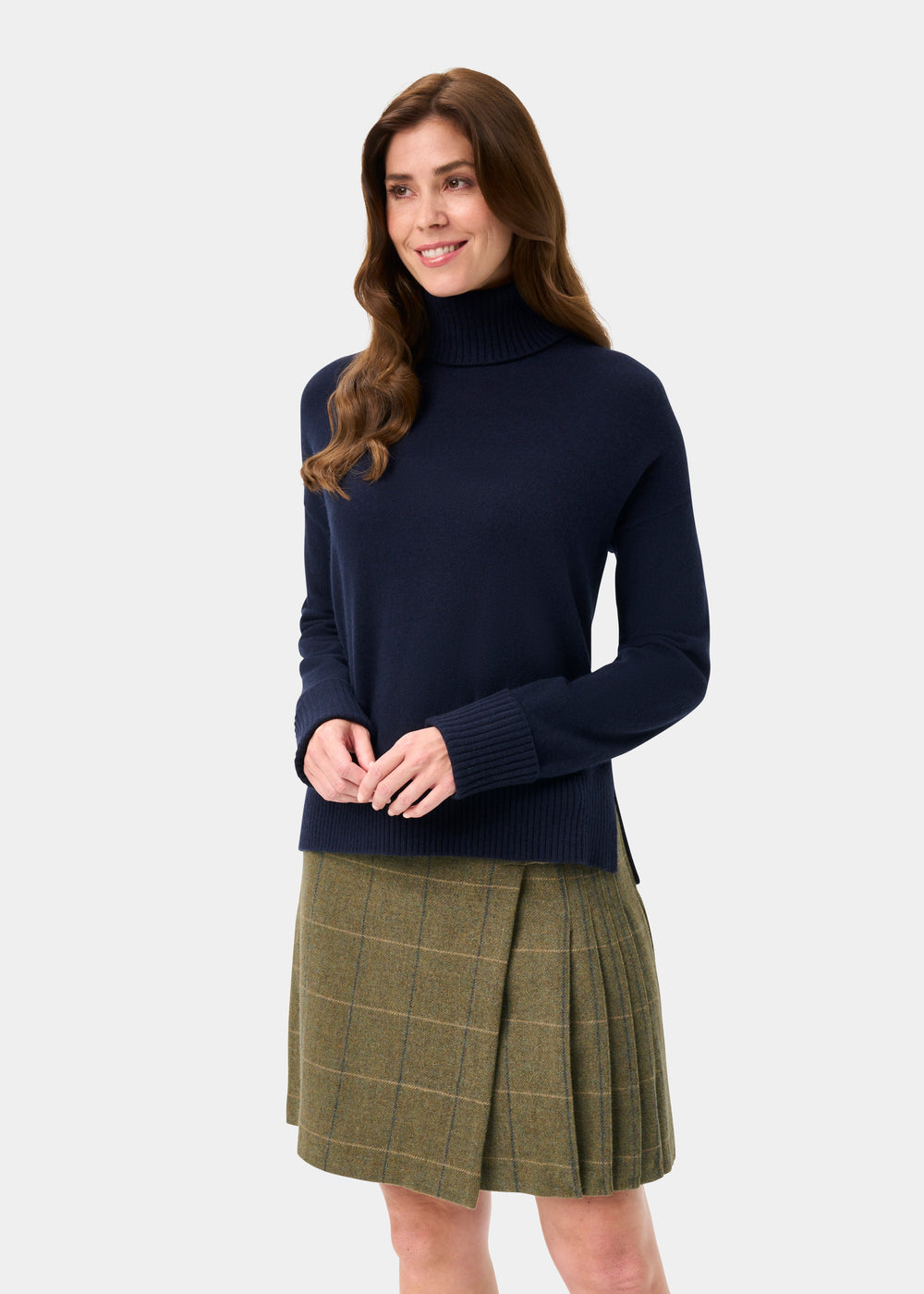 Woman in an Alexa Wool & Cashmere Roll Neck Jumper in dark navy and green plaid skirt, smiling.