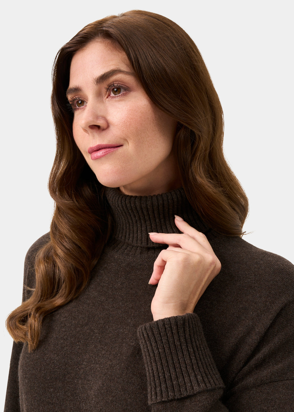 Woman with long brown hair wears the Alexa Wool & Cashmere Roll Neck Jumper in Walnut, touching her collar softly.