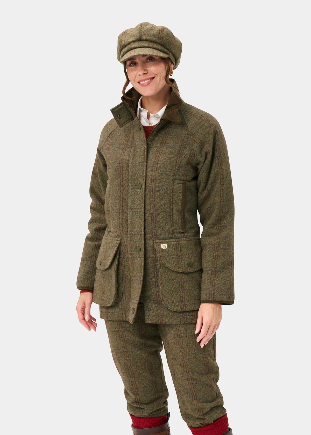 Woman in Combrook Ladies Tweed Waterproof Shooting Coat in Laurel, smiling against a plain white background.