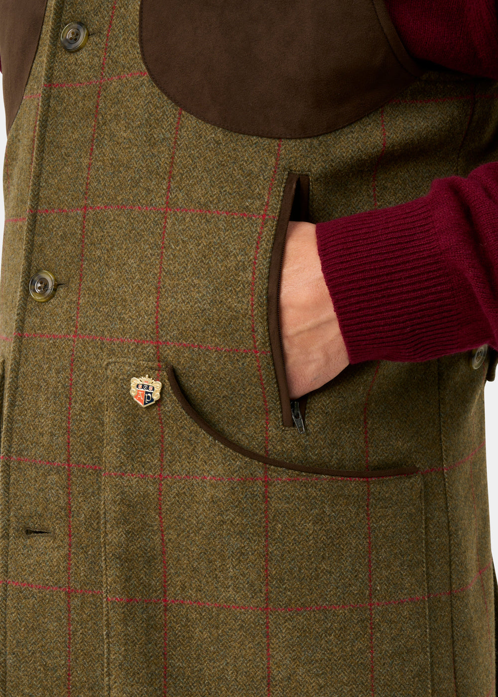 Hand in pocket of Combrook Men’s Sage Tweed Water Repellent Shooting Gilet, featuring brown and red details with crest pin.