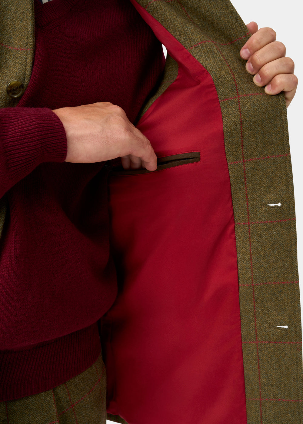 Hand opens Combrook Men’s Sage Tweed Shooting Gilet, revealing inner zip pocket and water repellent red lining.