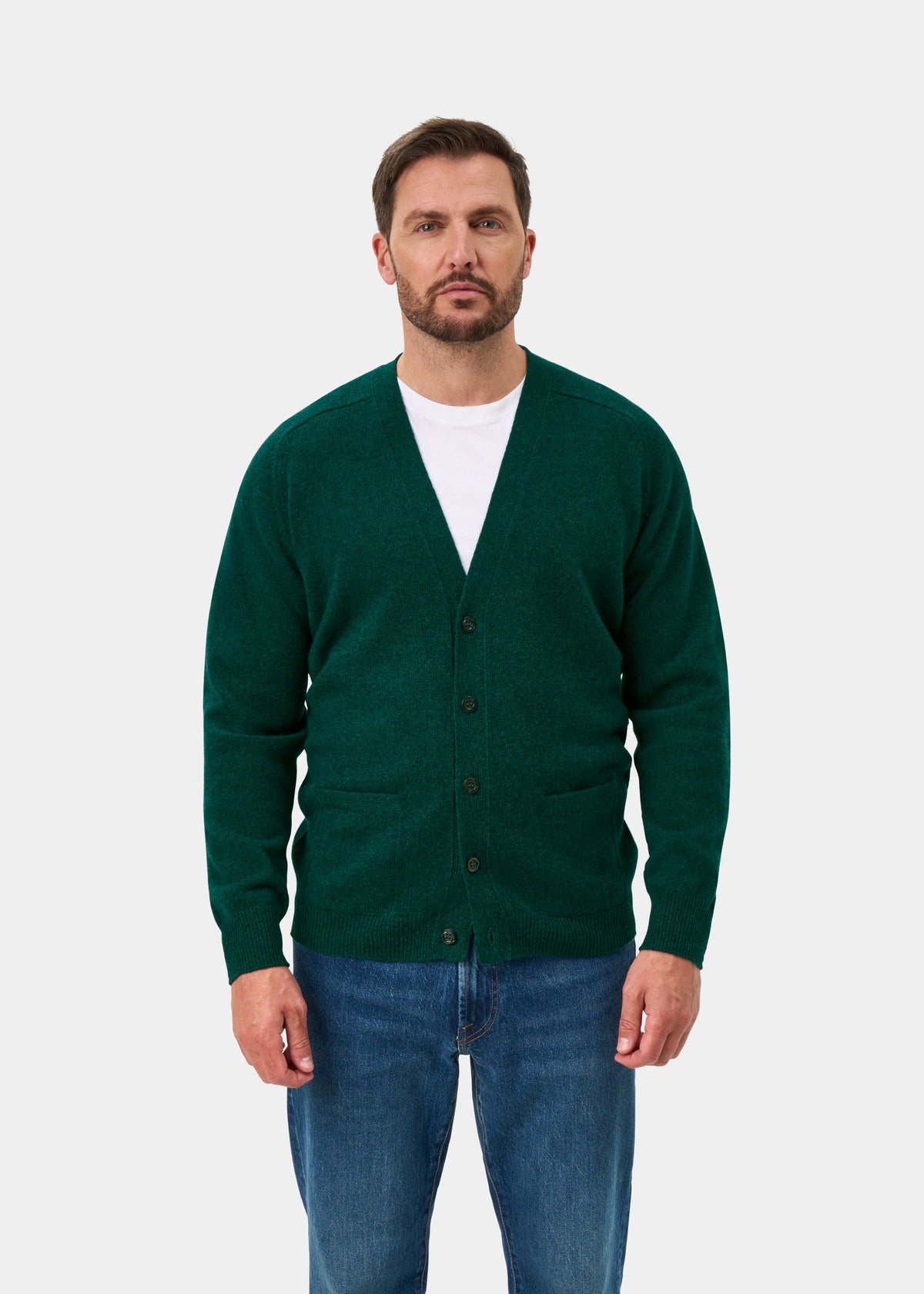 Man in Cornwall Lambswool V-Neck Cardigan in Mallard, white shirt, and blue jeans against a plain background.