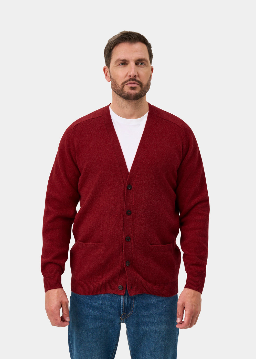A man wears the Cornwall Lambswool V-Neck Cardigan in Poppy Melange, white shirt, and jeans against a plain background.