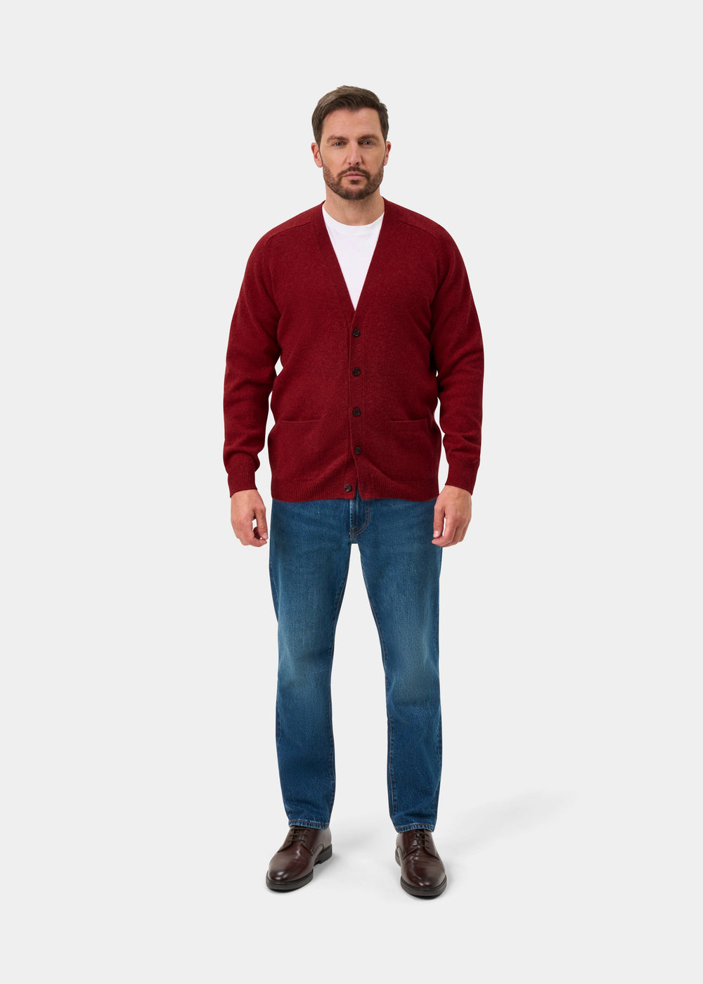 Man wearing Cornwall Lambswool V-Neck Cardigan in Poppy Melange over white tee, blue jeans, brown shoes.