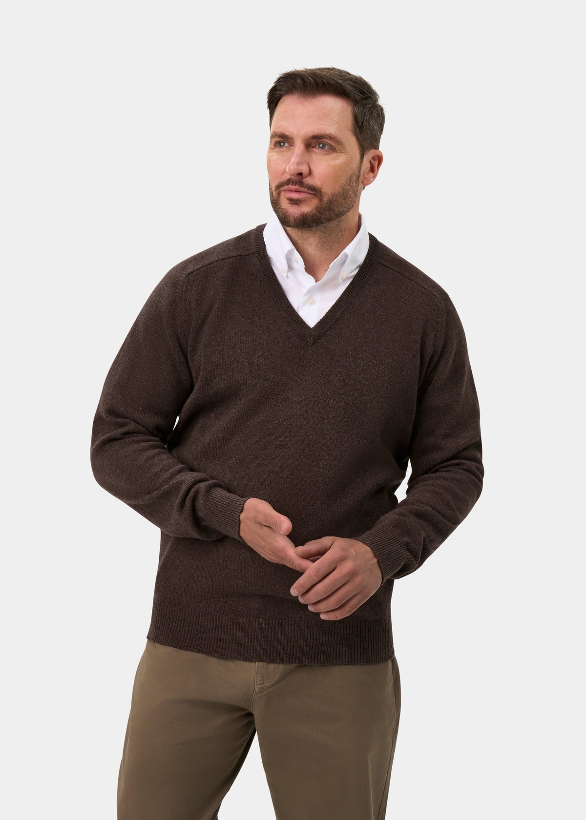 Man wears the Hampshire Lambswool V-Neck Jumper in Mocha—classic fit—paired with khaki pants, gazing to the side.
