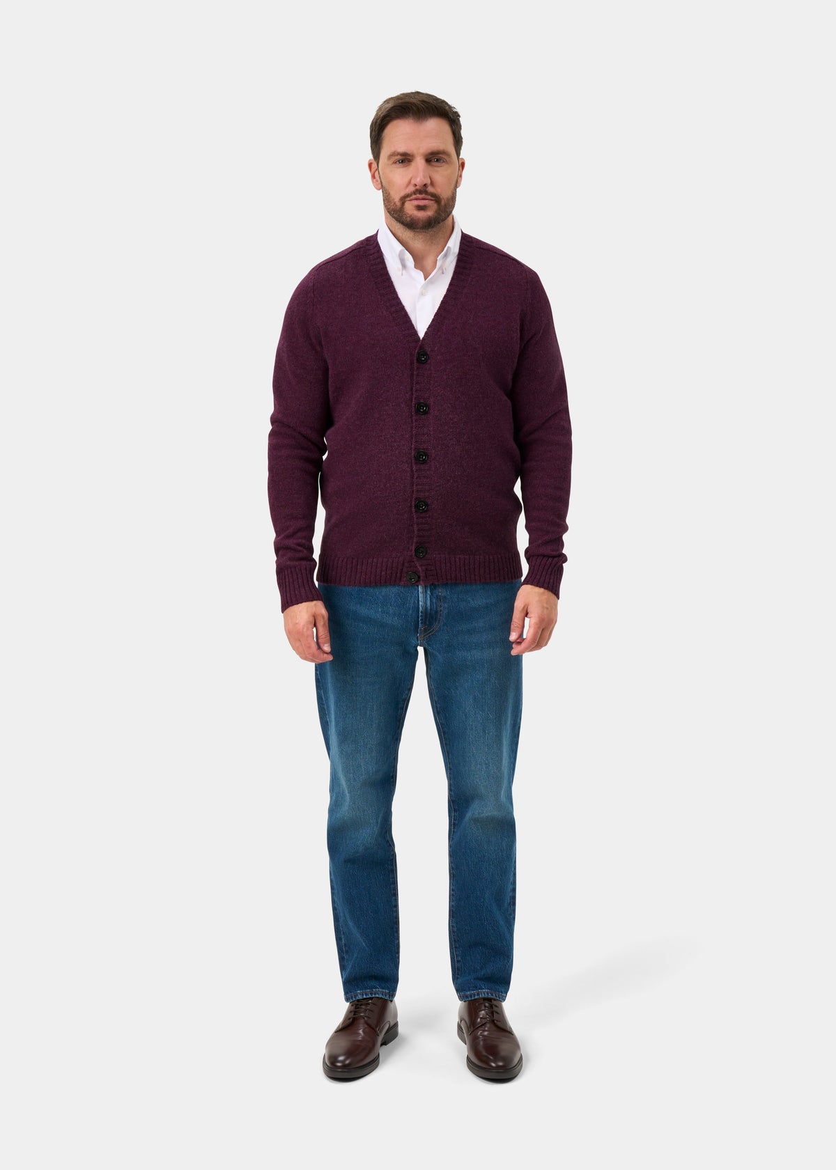 Man in a Kinloch Elderberry Supersoft Shetland Wool V-Neck Cardigan, white shirt, and blue jeans faces forward.