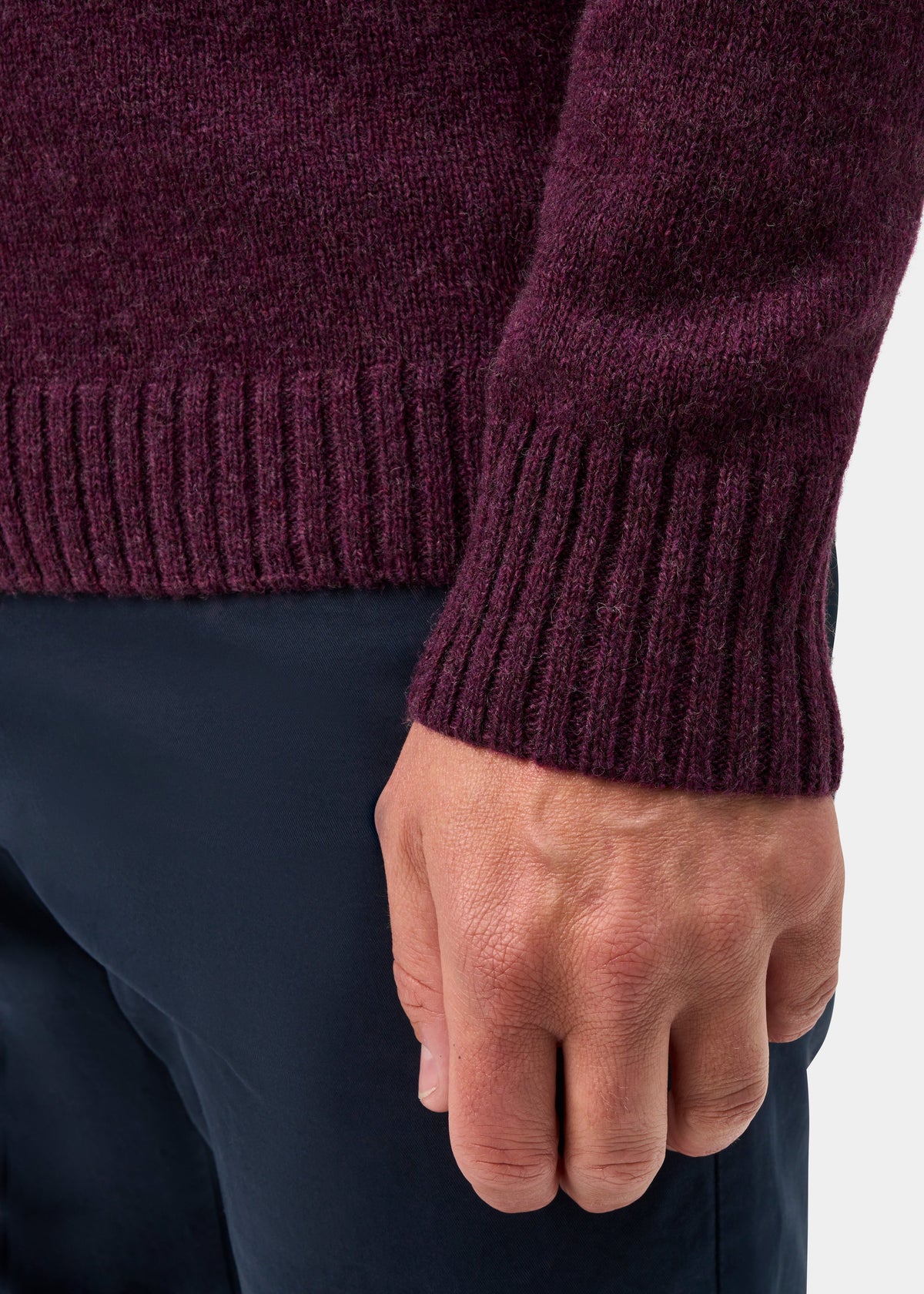 A person wears a Kinloch Supersoft Shetland Wool V-Neck Cardigan in Elderberry and navy pants, showing their hand.