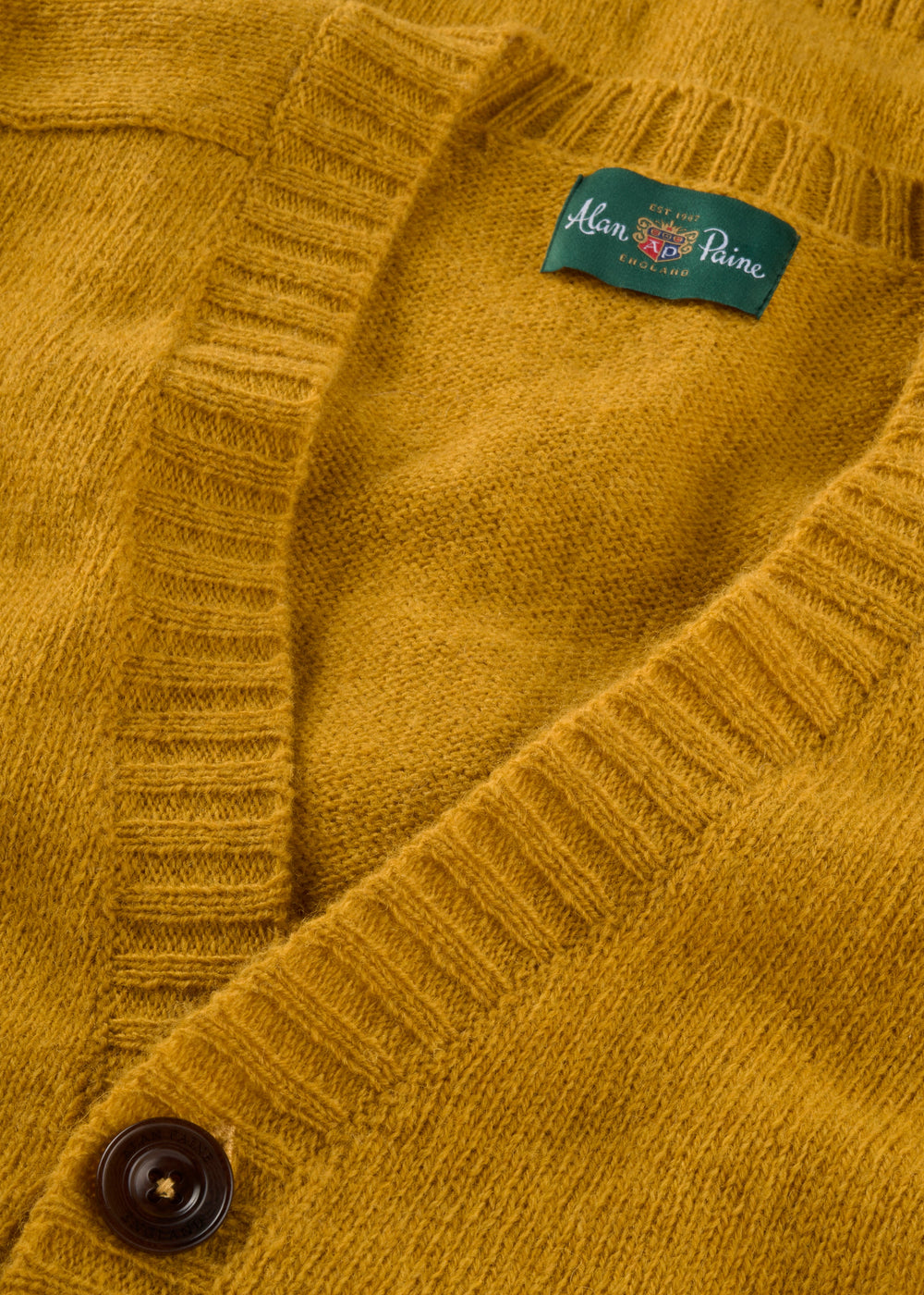 Close-up of Kinloch Supersoft Shetland Wool V-Neck Cardigan in Old Gold with button and visible brand label.