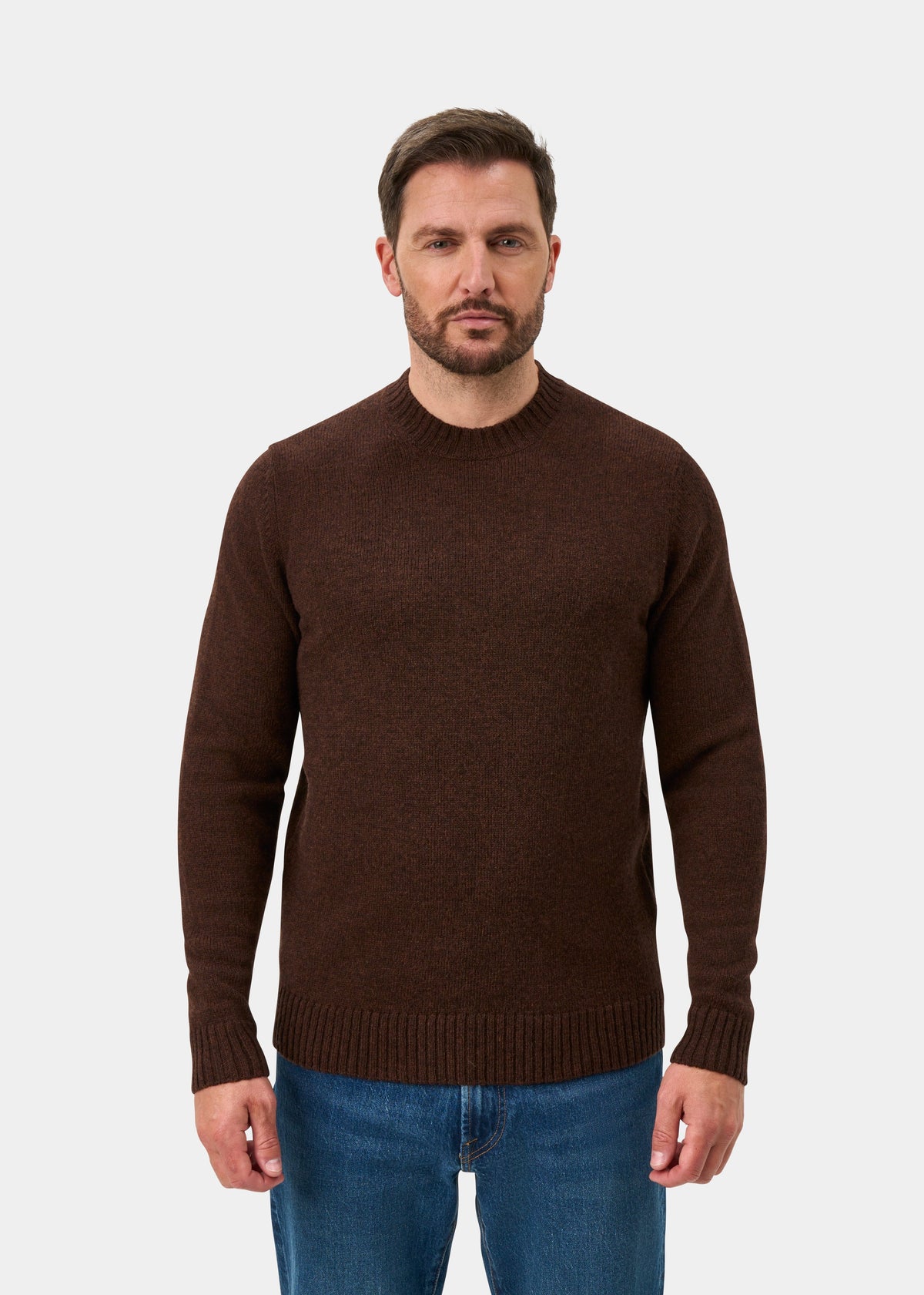 Man in coffee Kinnadie Supersoft Shetland Wool Crew Neck Jumper, blue jeans, stands facing forward against white background.