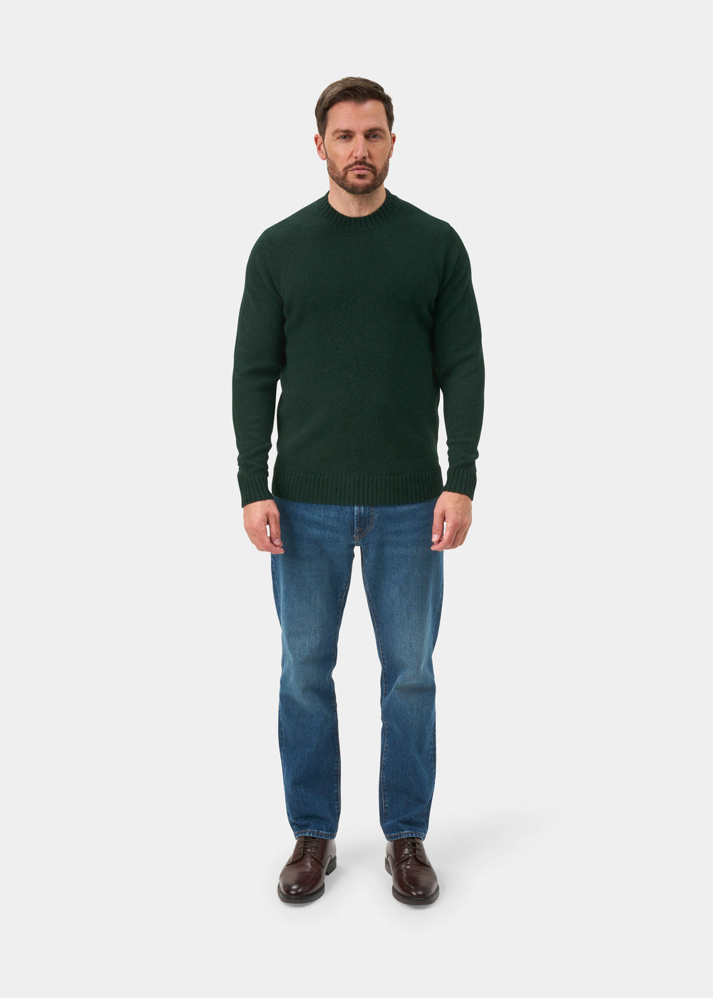 Man in a Kinnadie Supersoft Shetland Wool Crew Neck Jumper in Cossack, blue jeans, and brown shoes on white background.