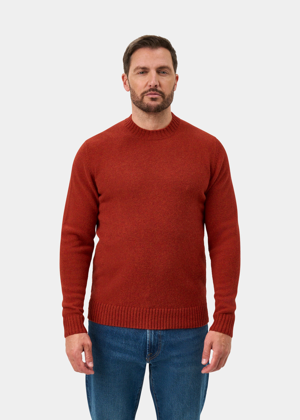 Man wearing Kinnadie Supersoft Shetland Wool Crew Neck Jumper in saffron and blue jeans stands against white background.