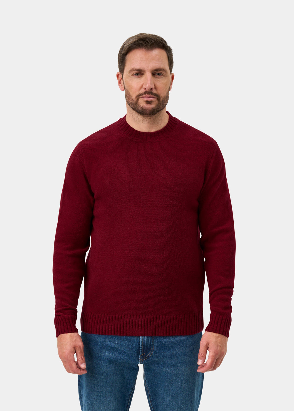 Man wears a Kinnadie Venetian wool crew neck jumper, regular fit, with blue jeans against a plain light background.