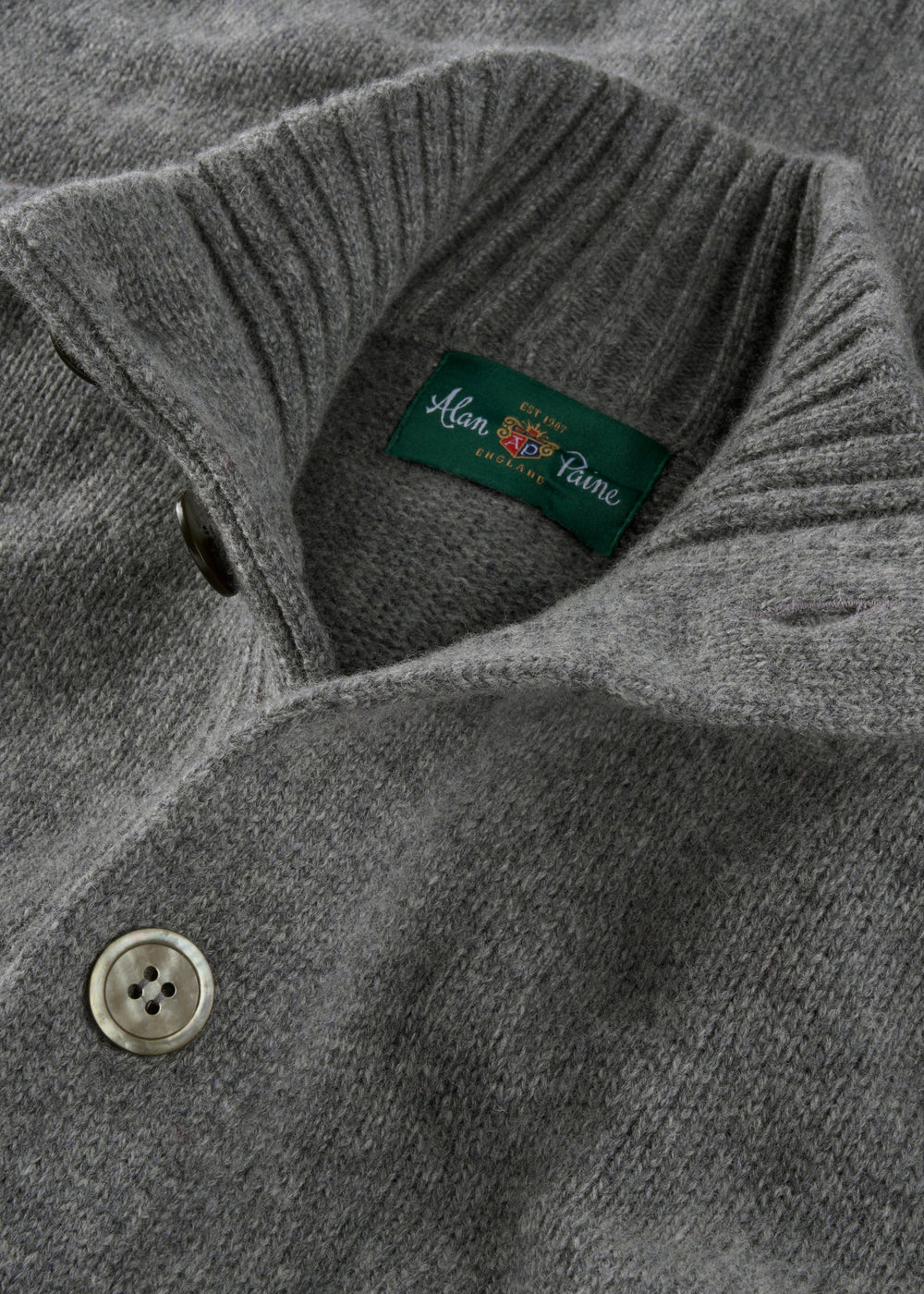 Close-up of the Landford Lambswool Buttoned Mock Neck Jumper in grey mix, with ribbed collar and green label.
