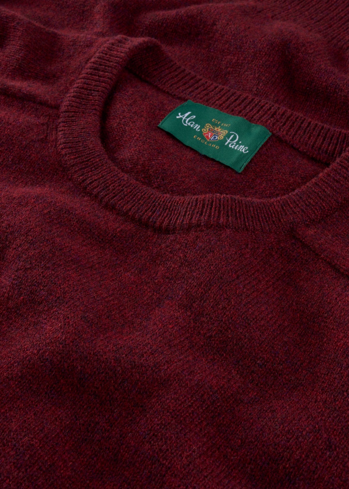 Close-up of the Lenzie Lambswool Crew Neck Jumper in Red Velvet, featuring a green Alan Paine England label.
