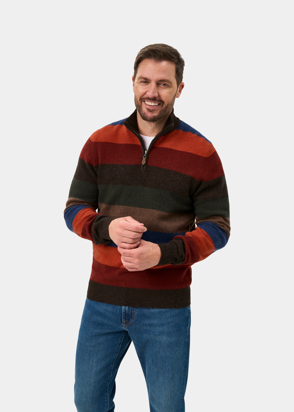 A man wearing a multi-colored striped quarter-zip sweater with blue jeans, standing against a light gray studio background.